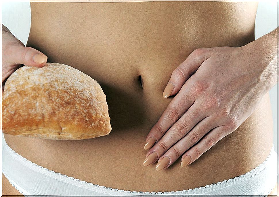 Woman with a bread in her hand and a tummy ache due to non-celiac gluten sensitivity.