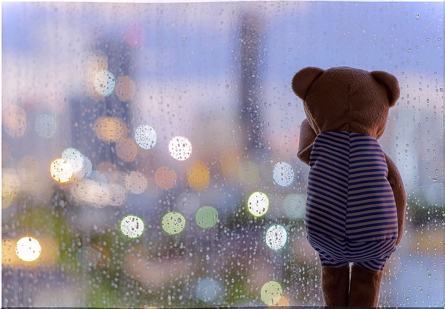 Teddy bear looking at the rain through the window.